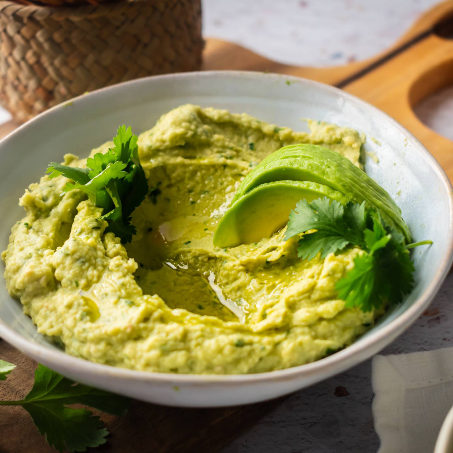 Avocado hummus in a bowl with cilantro and sliced fresh avocado.