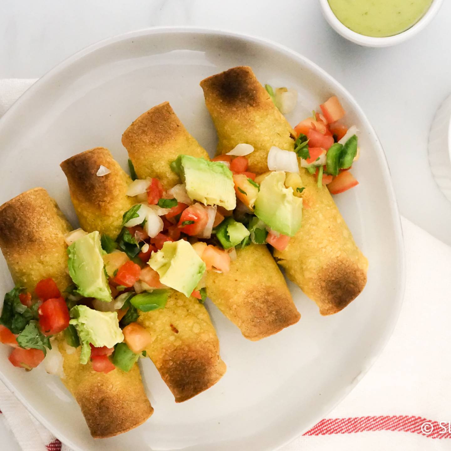 Chicken Taquitos on a plate with pico de gallo and avocado.