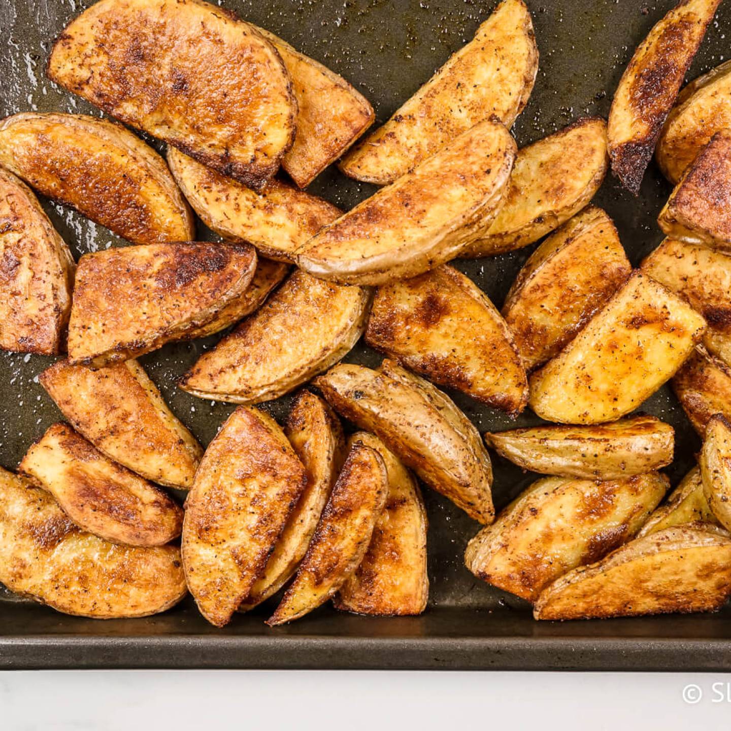 Crispy baked potato wedges on a cooking sheet with paprika, garlic powder, salt, and pepper.