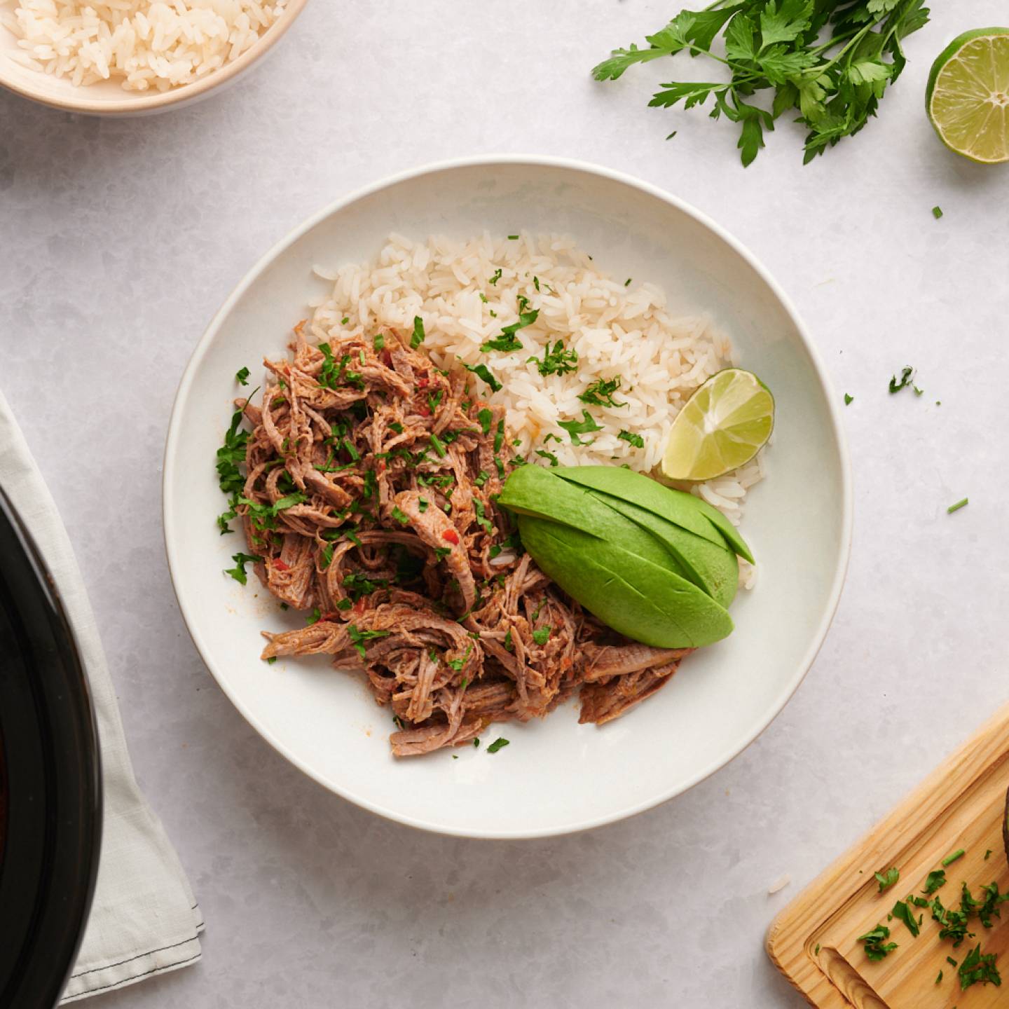 Beef machaca served with white rice in a bowl with cilantro and avocado on top.