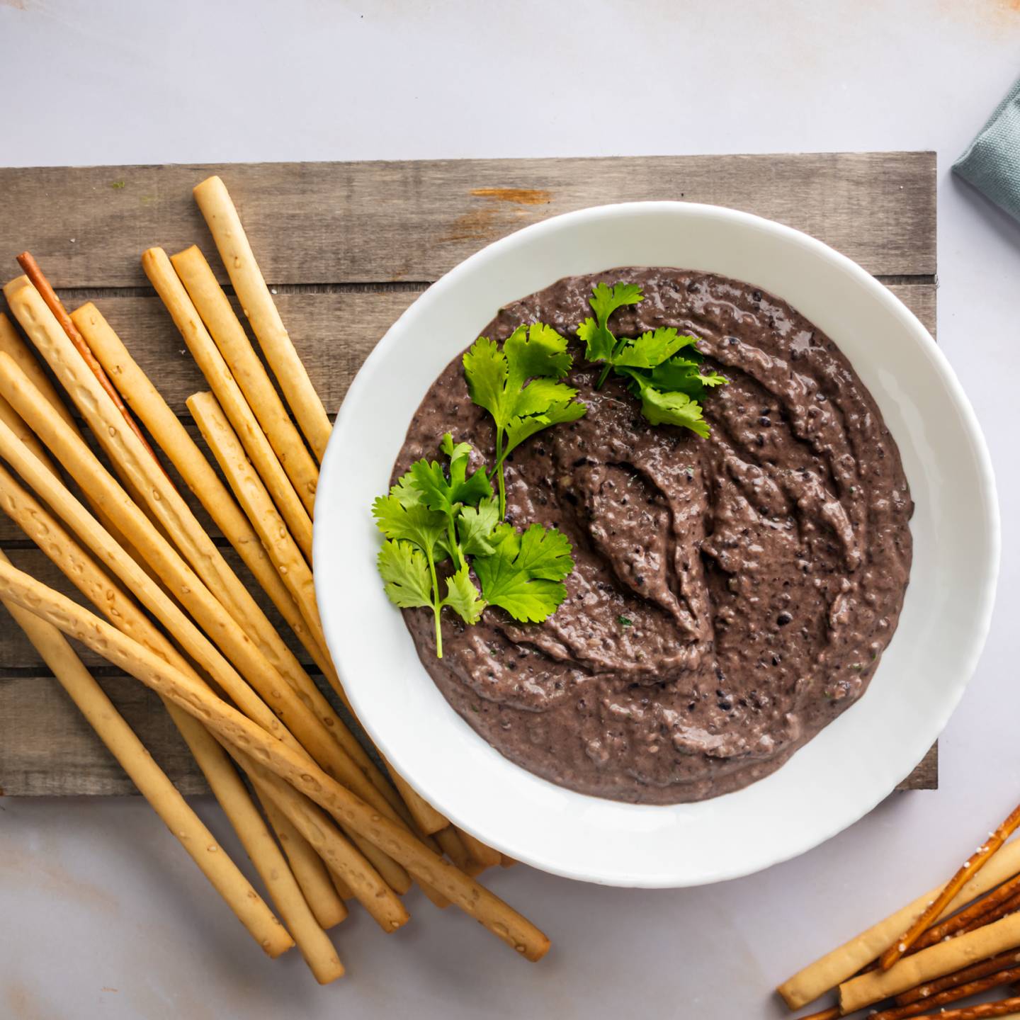 Black bean hummus in a bowl with cilantro with breadsticks and pretzels on the side.