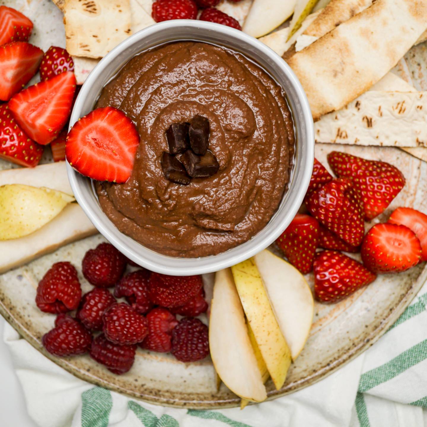 Brownie batter hummus in a bowl with cut fruit and crackers.