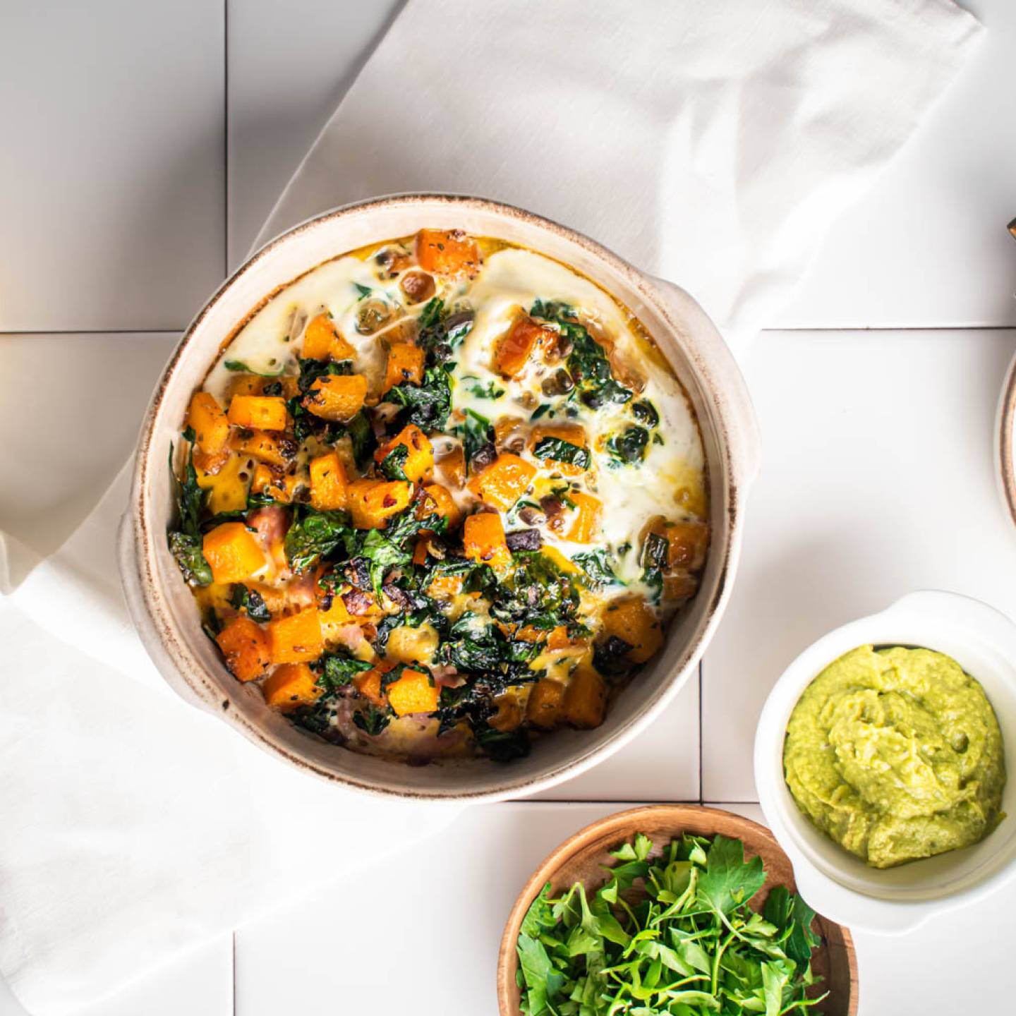 Butternut squash and egg breakfast casserole with turkey sausage in a baking dish with avocado on the side.