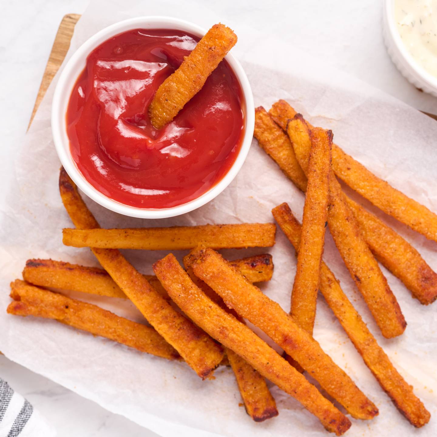 Butternut squash fries baked until crispy and served on parchment paper with ketchup and herb sauce.