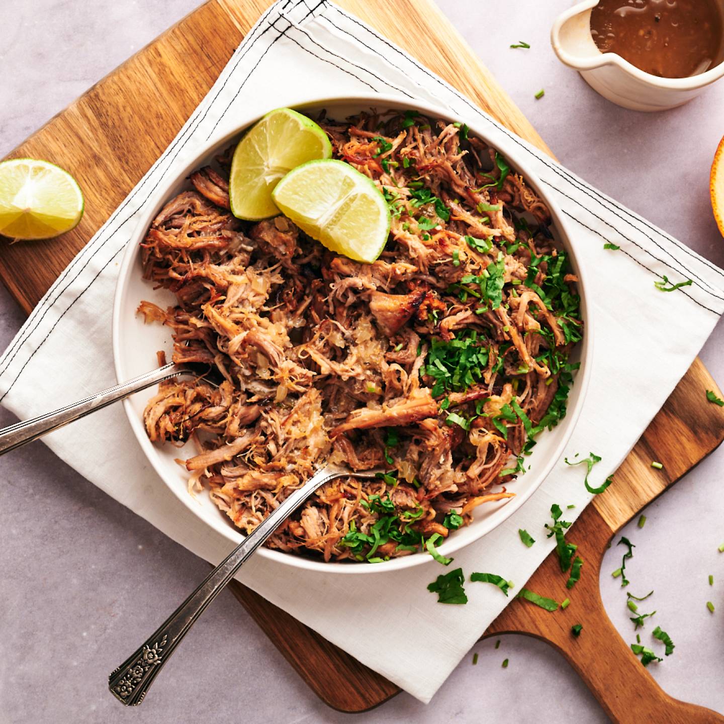 Carnitas served with shredded pork in a bowl with lime wedges, oranges, and cilantro.