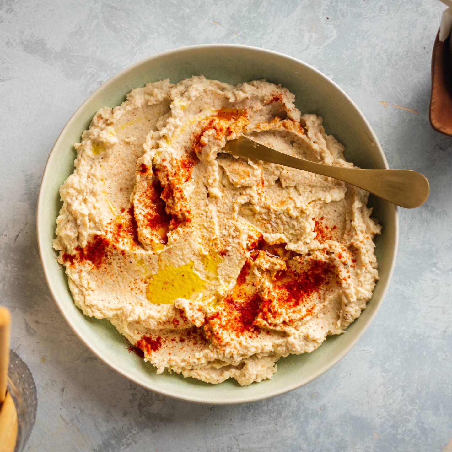 Cauliflower hummus with roasted cauliflower, tahini, olive oil, and lemon served in a bowl with breadsticks on the side.