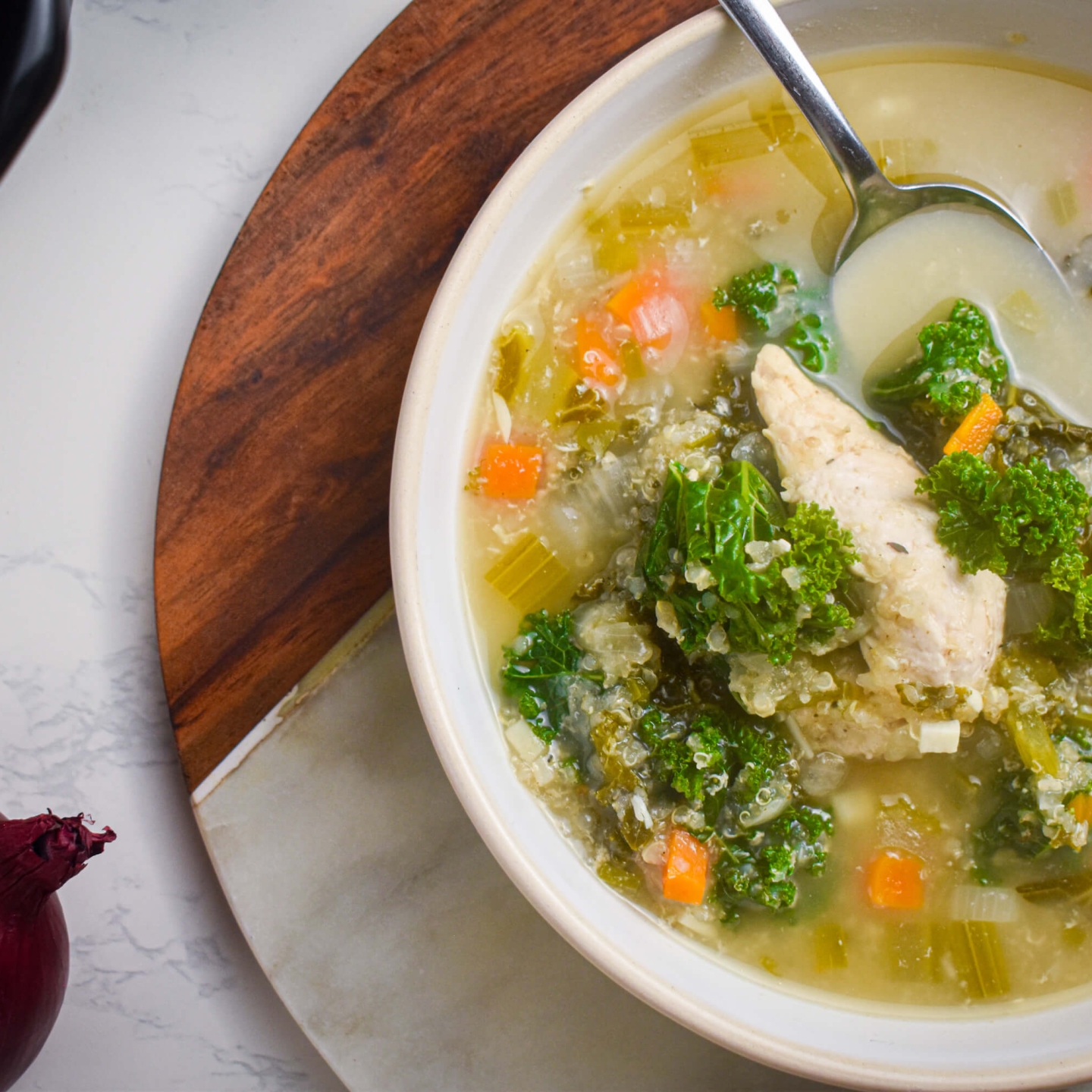 Slow cooker chicken quinoa soup with kale, carrots, celery, and onions in a bowl with a spoon.