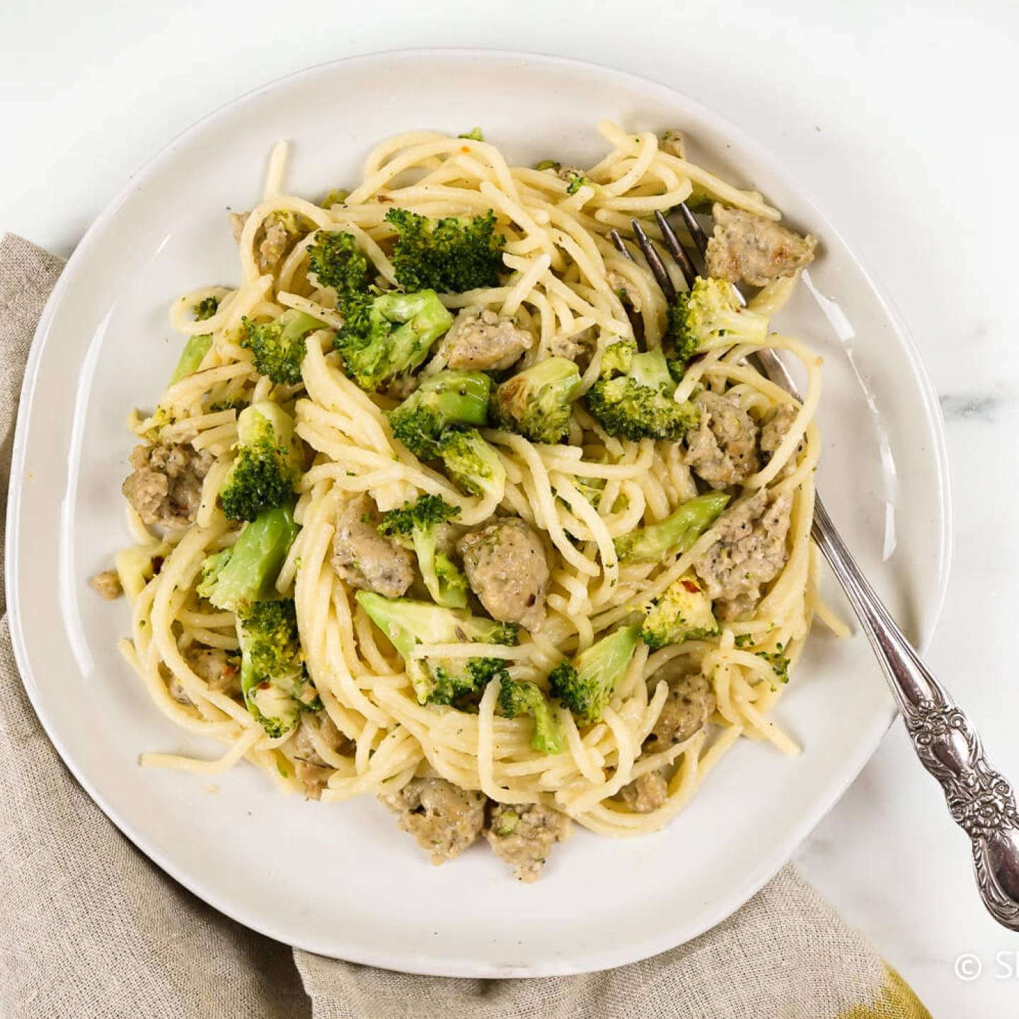 Chicken sausage pasta with broccoli on a plate with parmesan cheese and a fork.