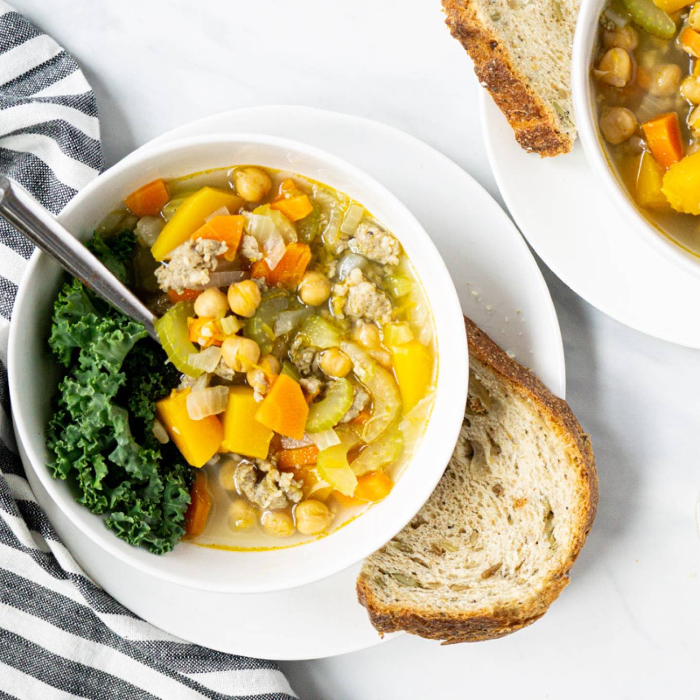 Chickpea stew with turkey sausage and butternut squash in a white bowl with bread on the side.