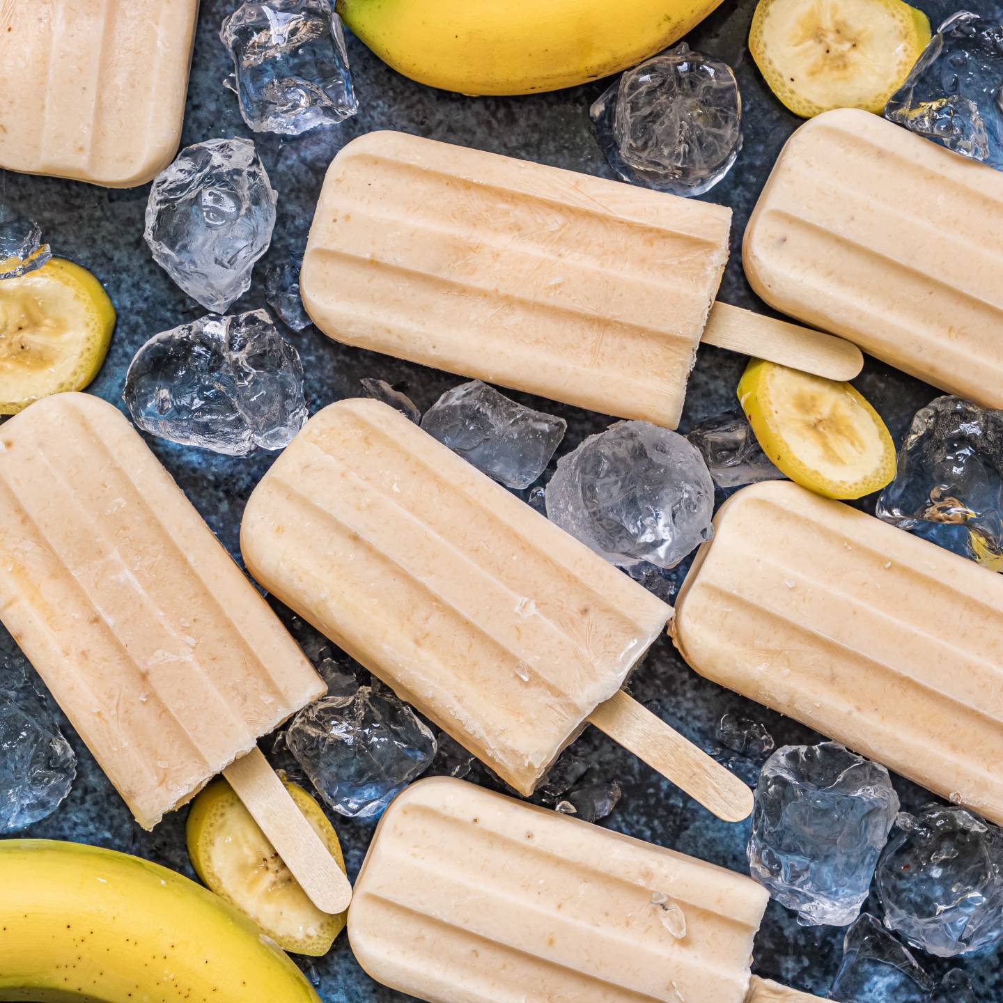 Banana popsicles with blended fresh bananas, yogurt, and honey on a marble board with banana slices. 