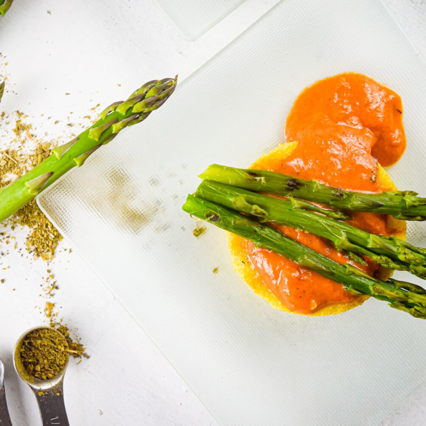 Crispy polenta with asparagus in a creamy tomato sauce on a clear plate with herbs.