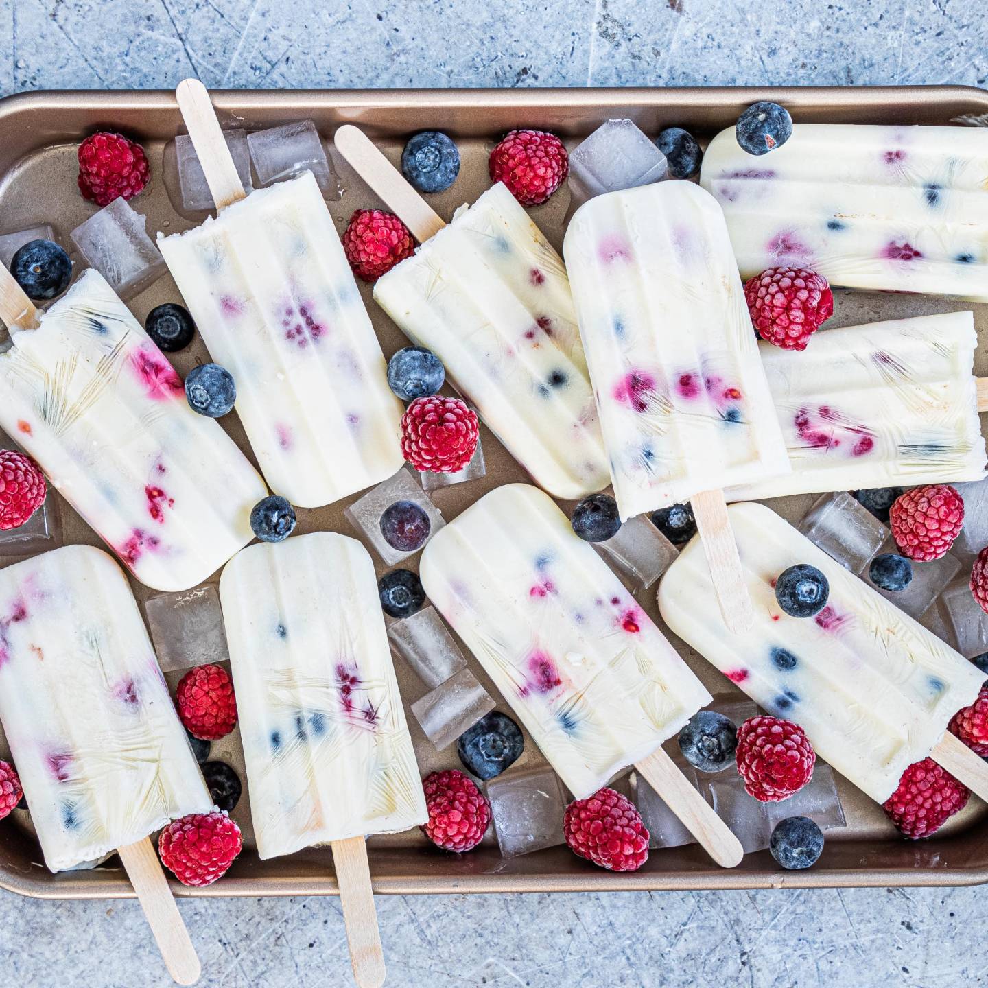 Fruit and yogurt popsicles with blueberries and raspberries on a tray with ice.