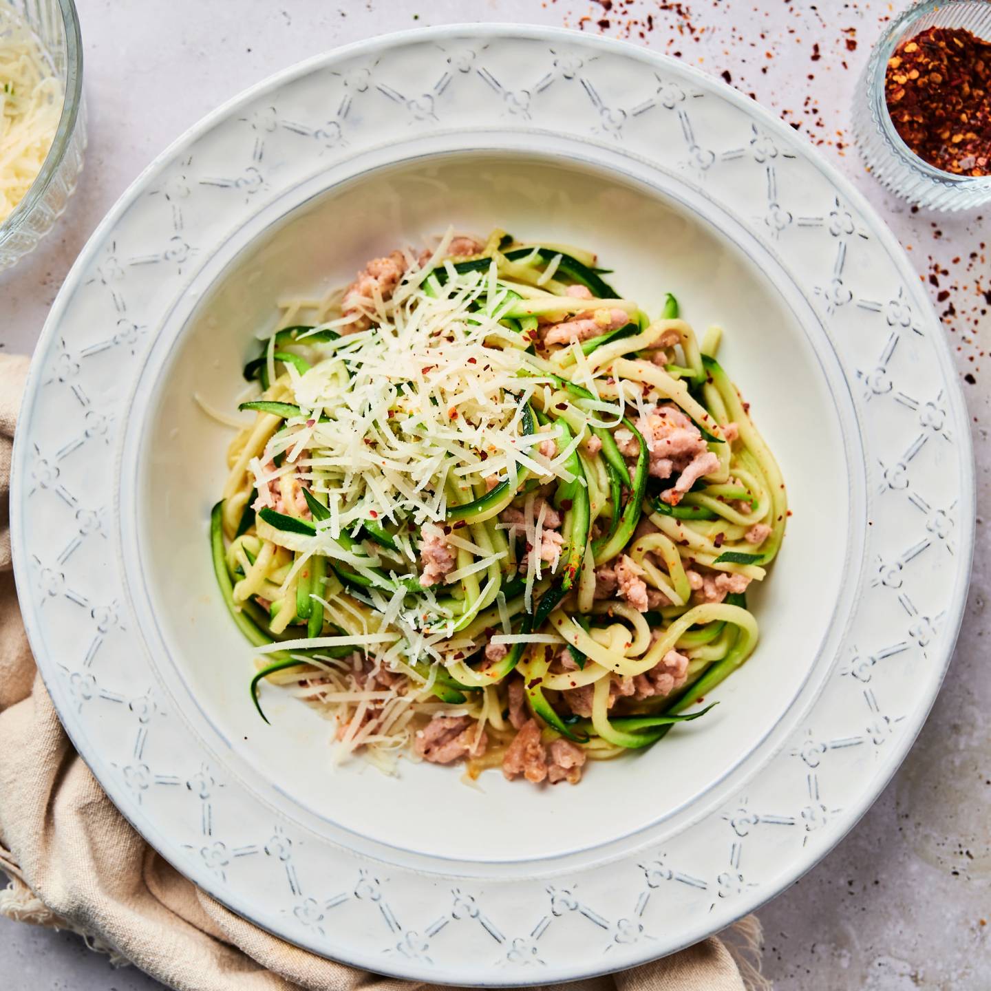 Garlic parmesan zucchini noodles with ground sausage and red pepper flakes in a white bowl.