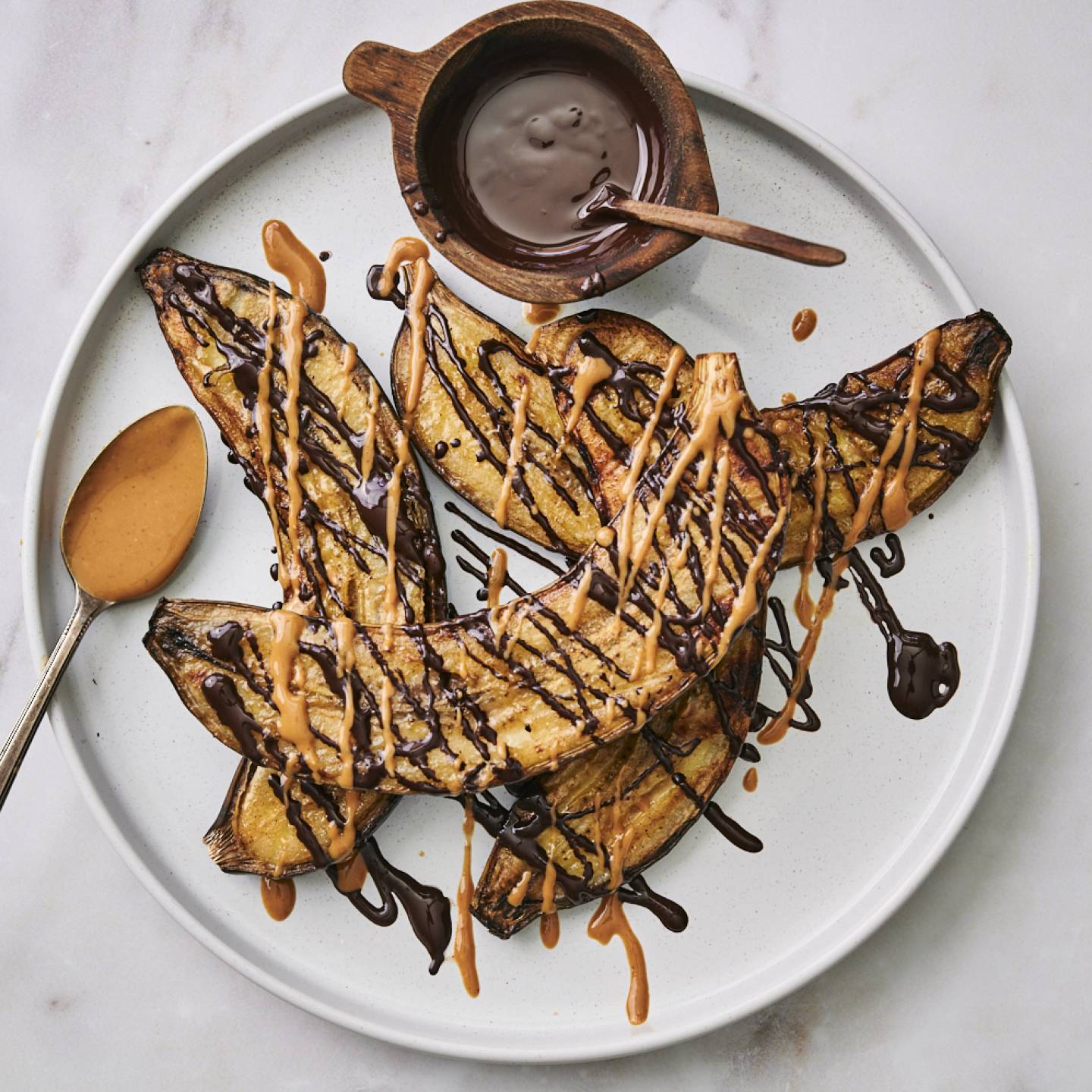 Grilled bananas on a plate with peanut butter, chocolate, and cinnamon. 