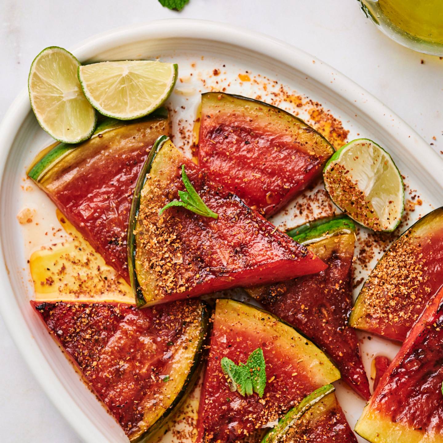 Grilled watermelon on a platter served with chili powder, lime wedges, and fresh mint.