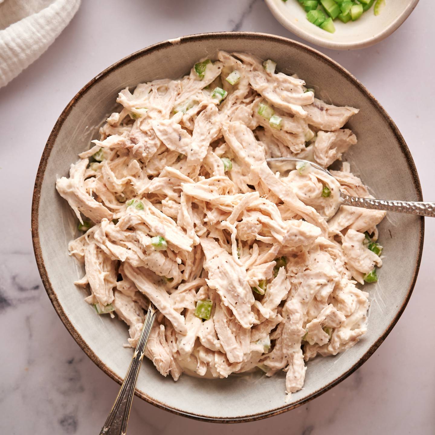 Healthy chicken salad with shredded chicken, celery, greek yogurt, mayonnaise, and spices in a bowl.