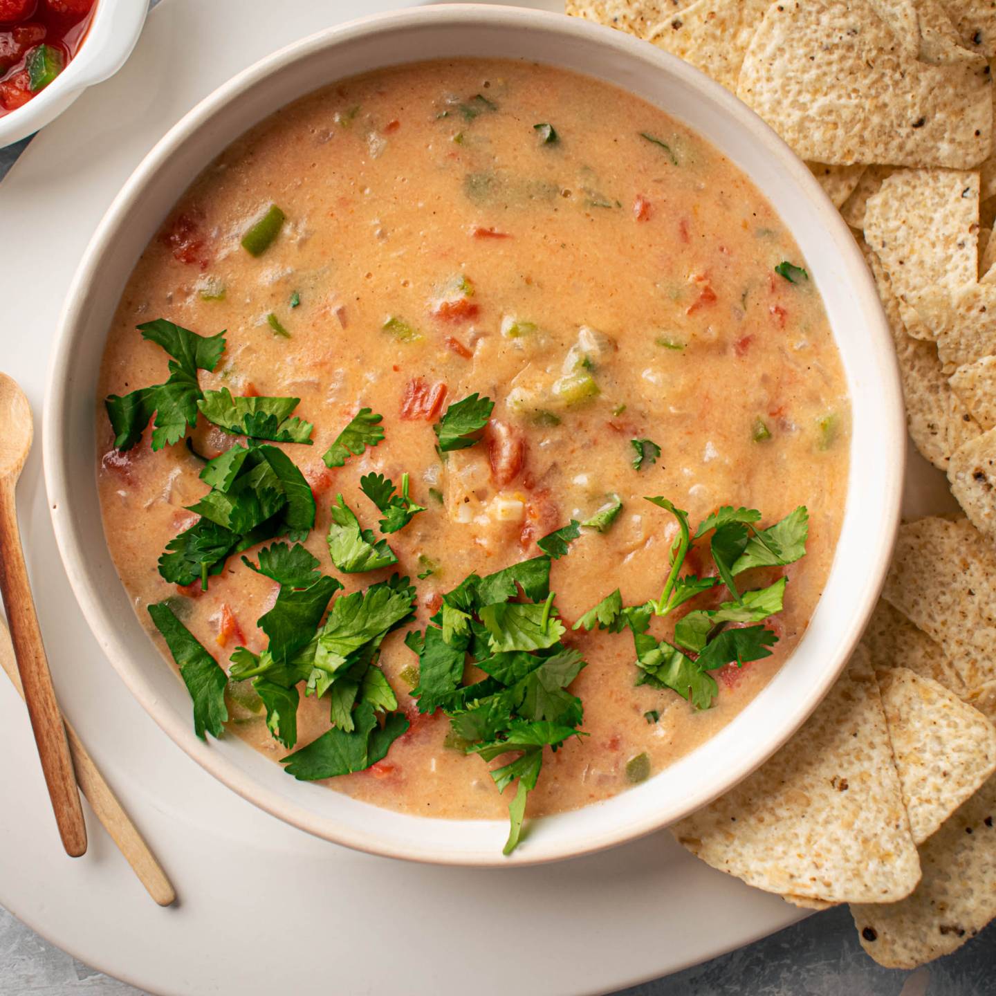 Healthy queso dip with melted cheddar cheese, diced tomatoes, and jalapeños in a bowl with tortilla chips.