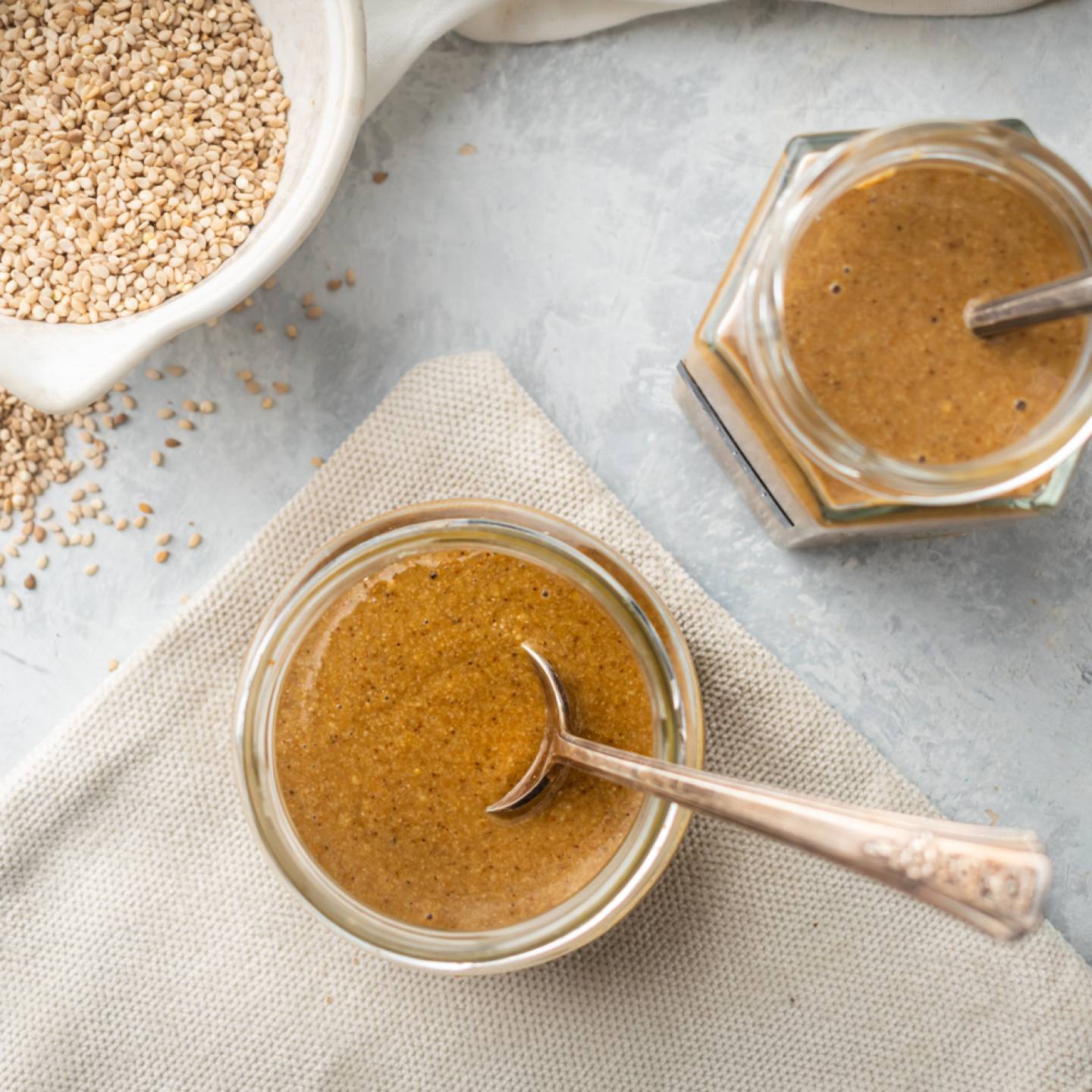 Homemade tahini with toasted sesame seeds and olive oil served in glass jars with spoons.