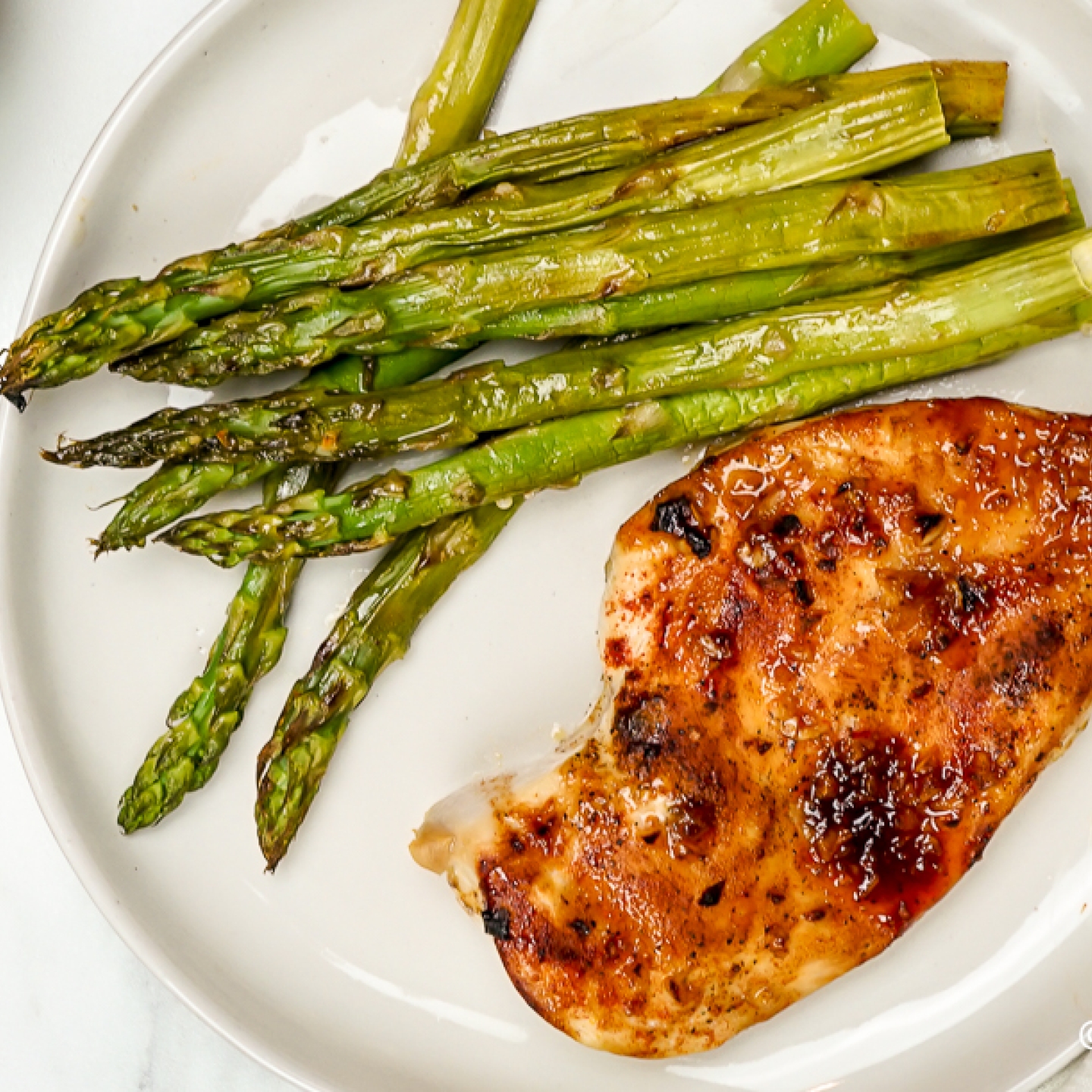 Honey garlic chicken on a plate with asparagus.