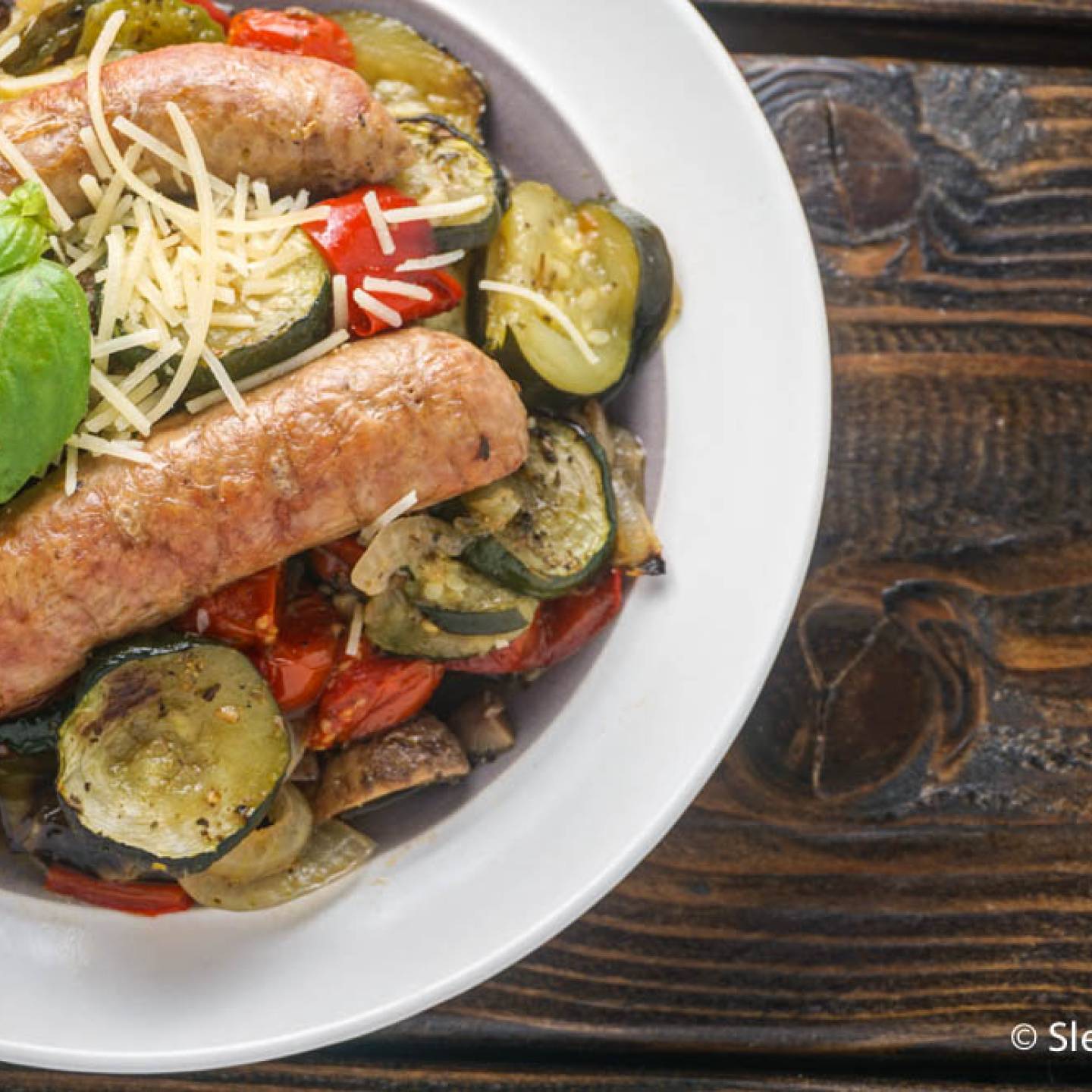 Italian sausages with tomatoes, zucchini, onions, and peppers in a bowl.