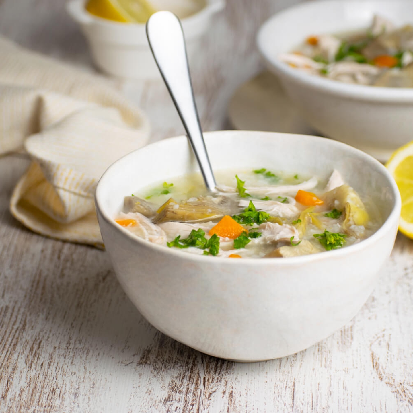 Slow cooker lemon artichoke chicken soup with quinoa in a bowl with carrots and lemon.