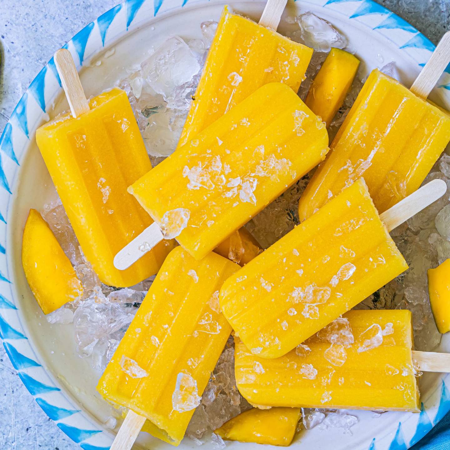 Mango popiscles made with fresh mango pieces, lime juice, water, and honey on a plate with ice.