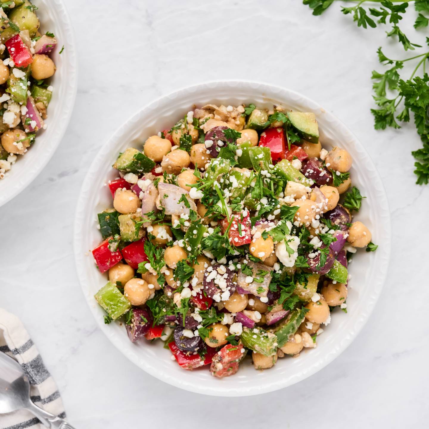 Mediterranean salad with chickpeas, olives, bell peppers, fresh herbs, and feta cheese in a bowl.