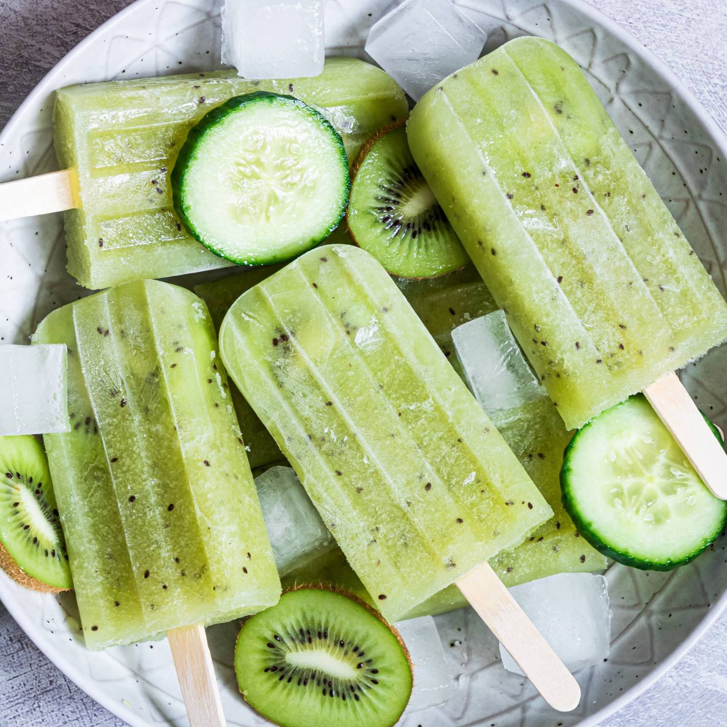 Mexican cucumber paletas with fresh kiwi and cucumber served on a plate with ice.