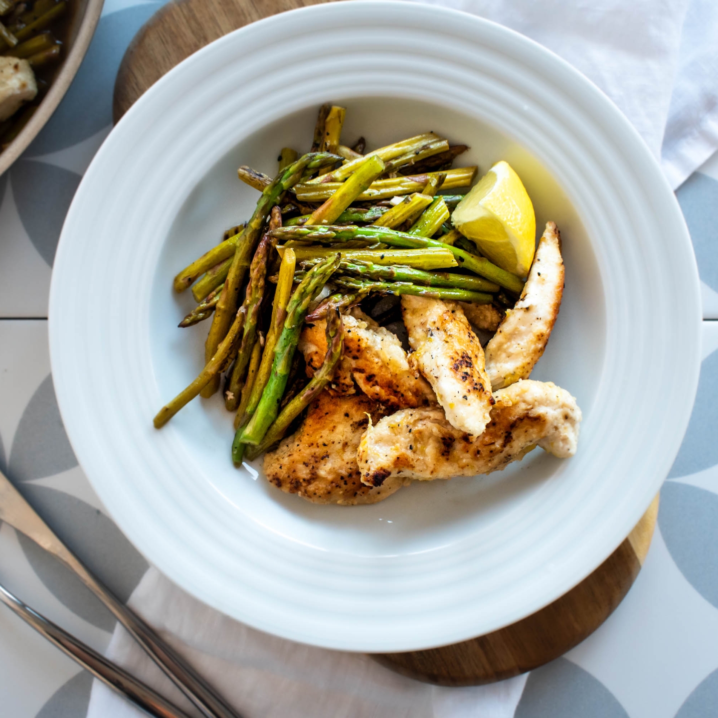 One pan lemon garlic chicken and asparagus served with fresh lemons in a bowl and in a skillet.