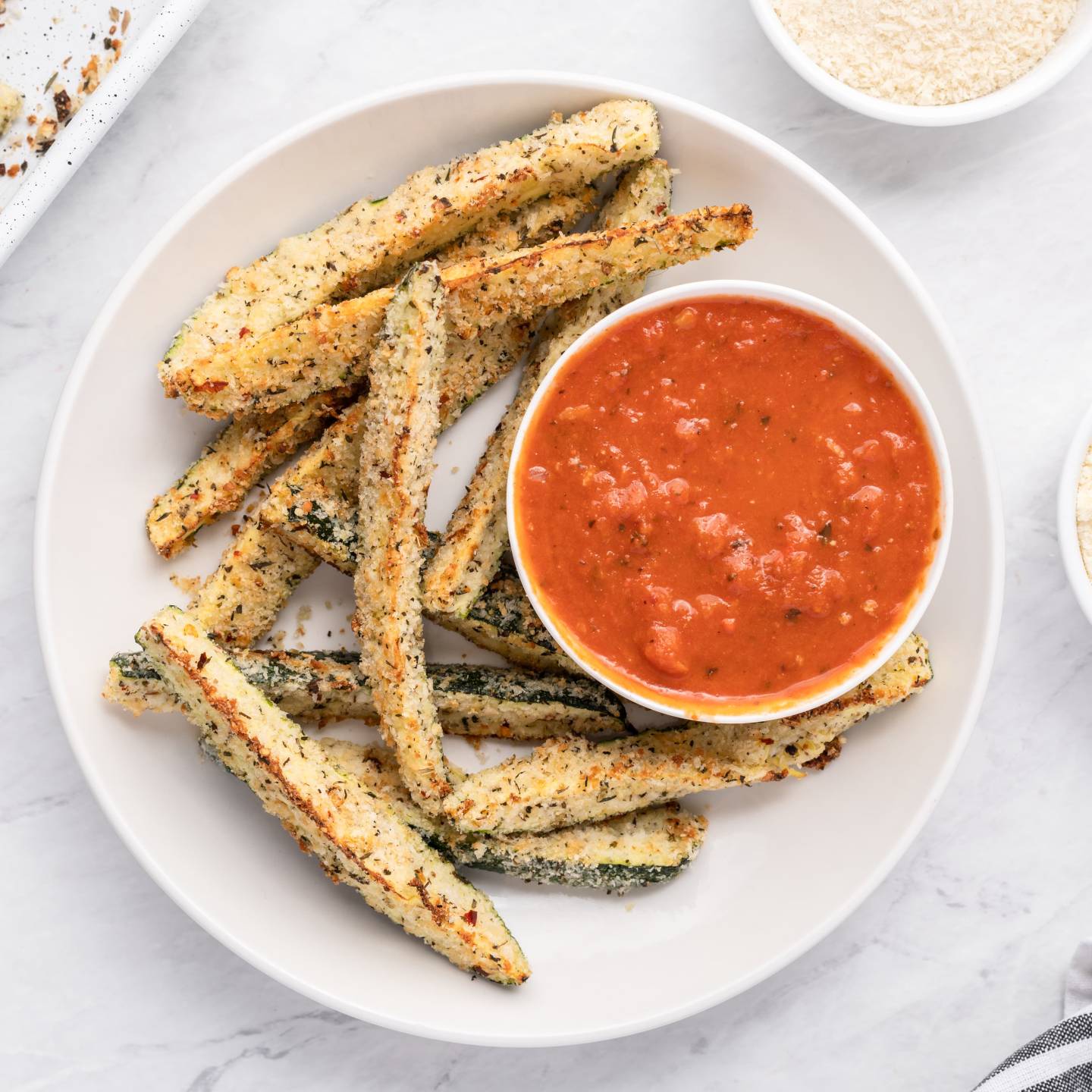 Baked Parmesan zucchini fries with a crispy panko breading on a white plate with marinara sauce.