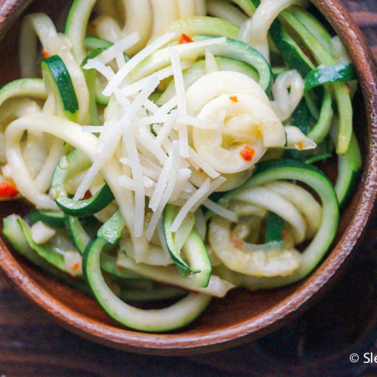 Parmesan zucchini noodles with shredded Parmesan cheese, red pepper flakes, and black pepper in a wooden bowl.