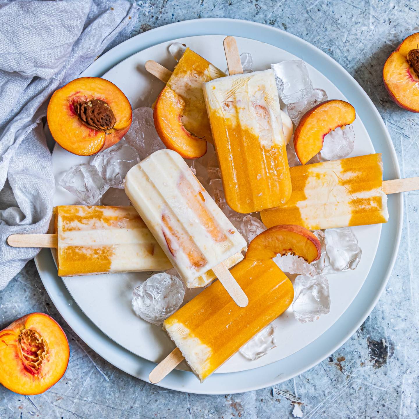 Peaches and cream popsicles with fresh peaches, honey, and Greek yogurt on a plate with ice and fresh peaches.