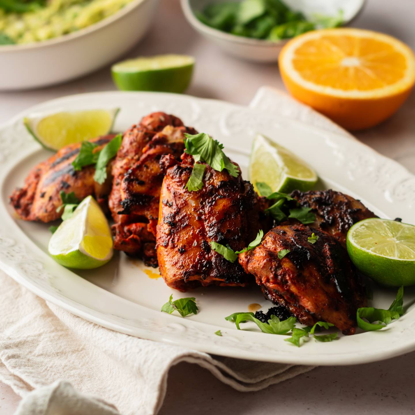 Pollo asado made with chicken thighs marinated in achiote paste and citrus juice served on a plate with guacamole and pickled onions.