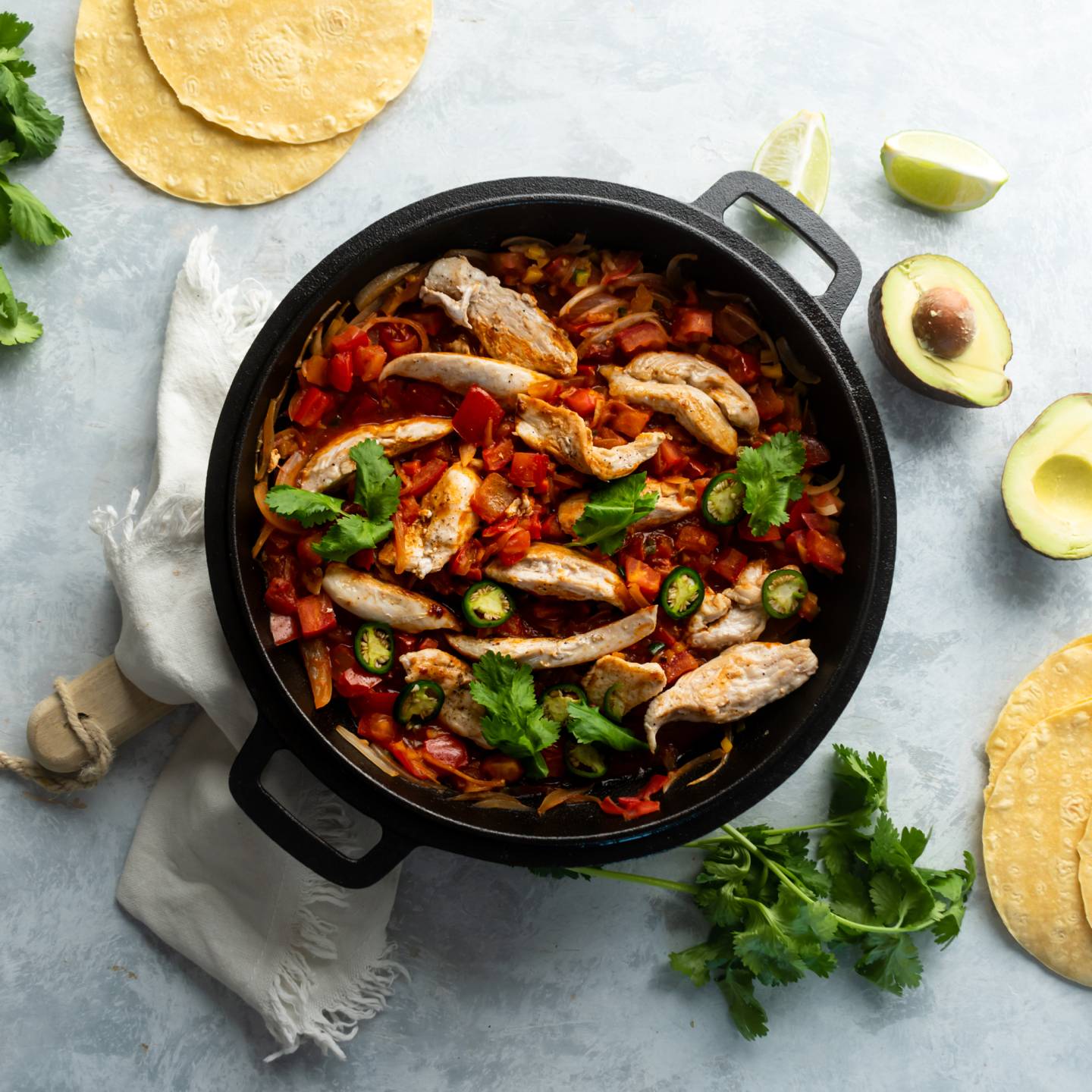 Pollo ranchero with chicken breast, tomato ranchero sauce, jalapeños, and cilantro in cast iron skillet.