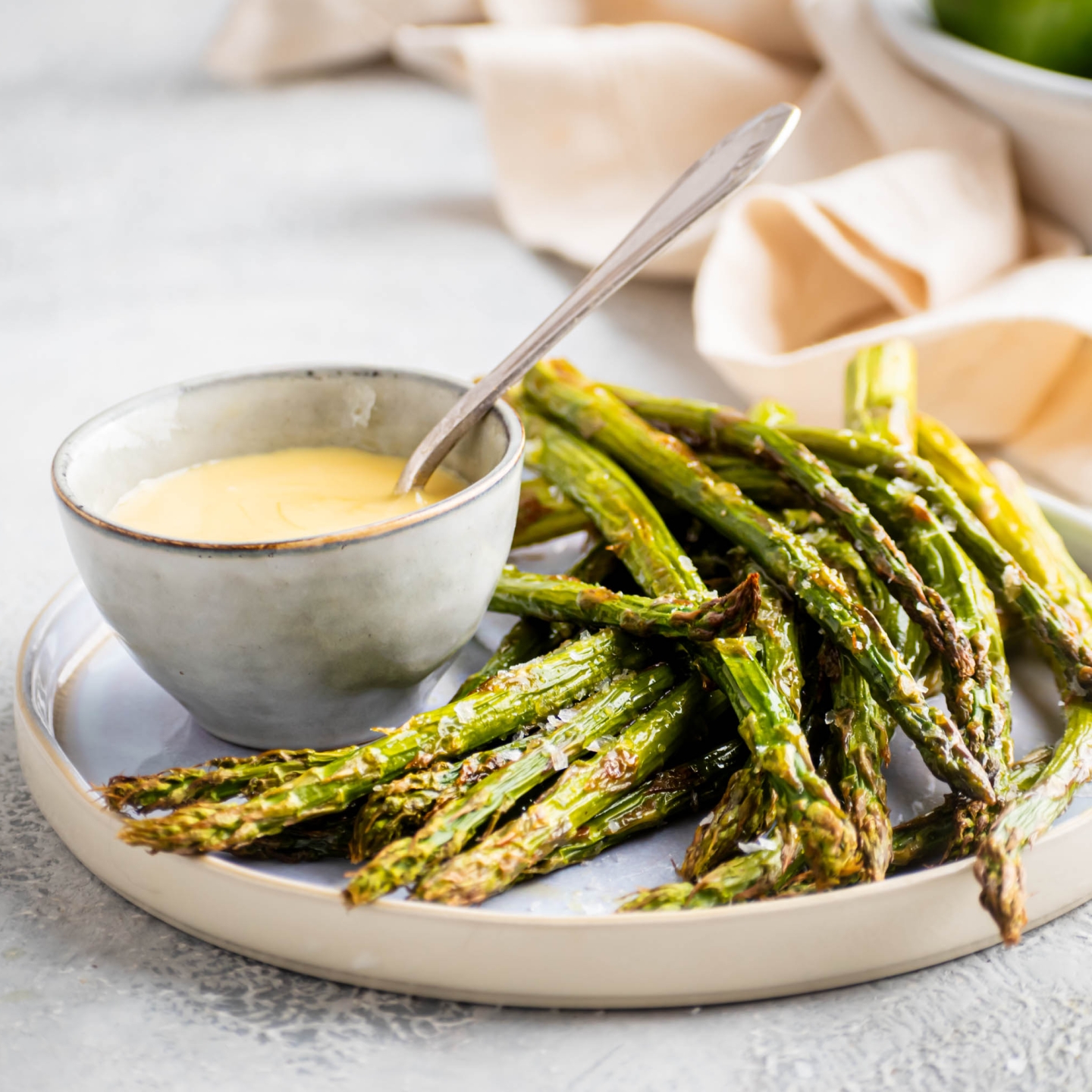 Roasted asparagus with olive oil, salt, and pepper served on a plate with hollandaise sauce.