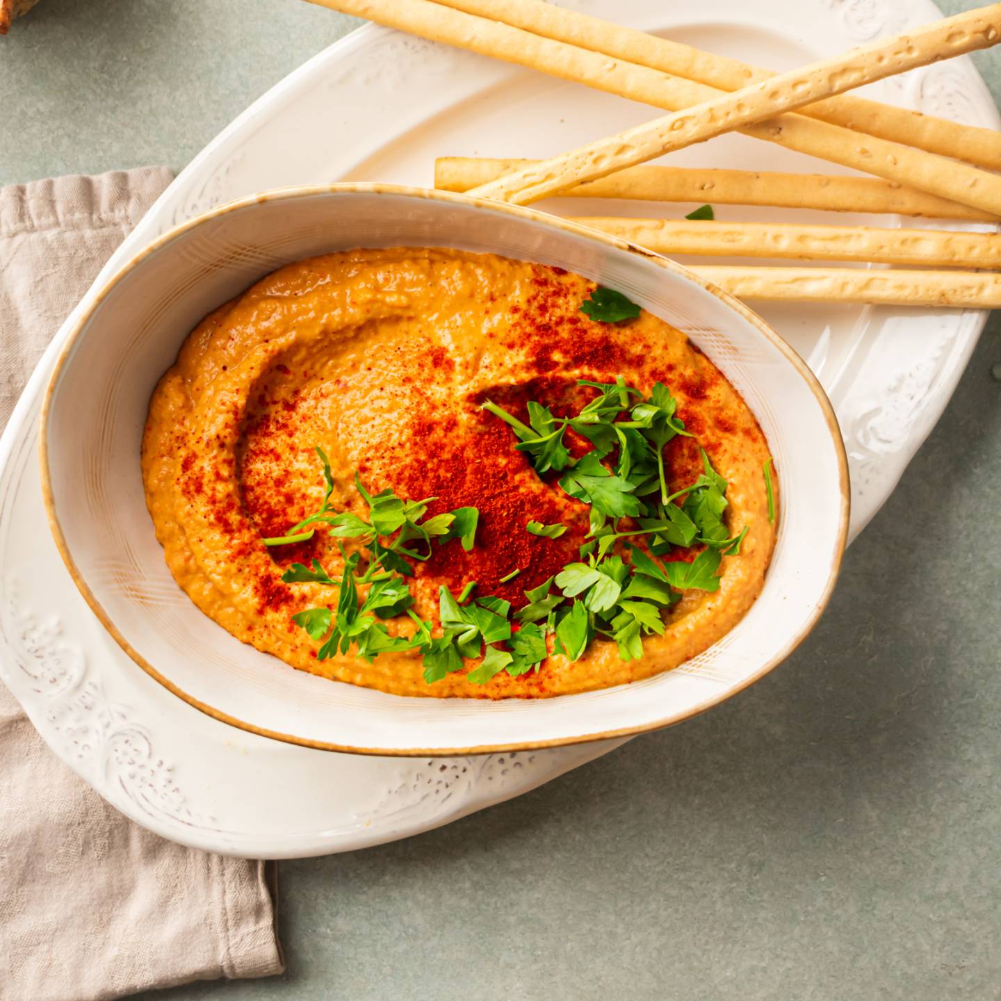 Roasted red pepper hummus made with chickpeas, tahini, garlic, lemon, and olive oil in a bowl with cilantro and paprika.