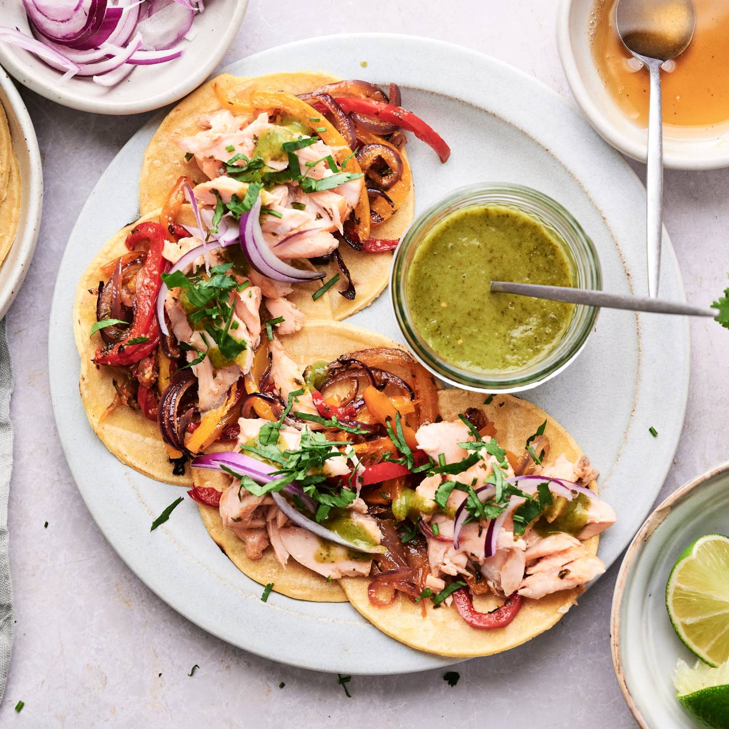 Salmon fajitas with flaked salmon, peppers, onions, cilantro, and green salsa served in corn tortillas.