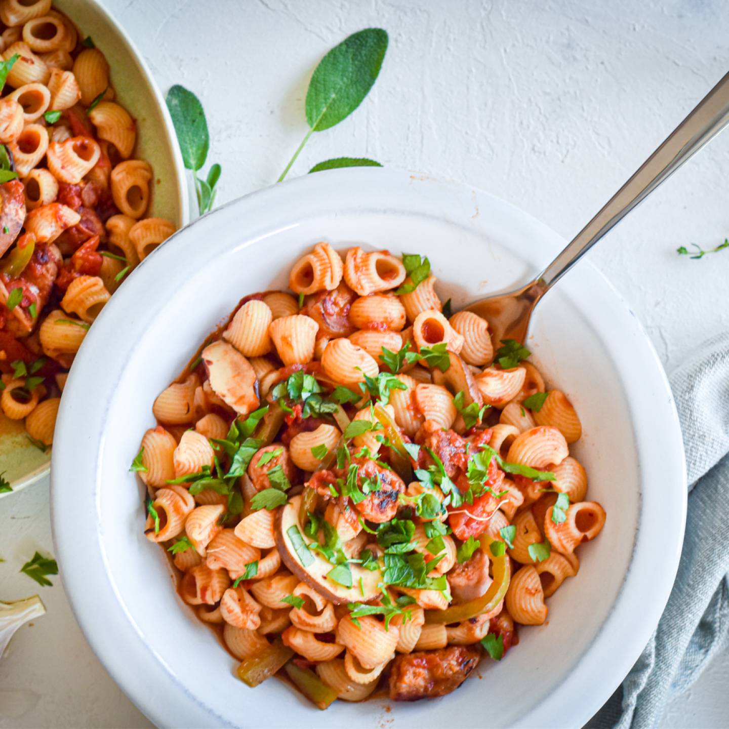 Sausage and pepper pasta with turkey sausage, bell peppers, onions, mushrooms, and tomato sauce in two bowls with garlic.