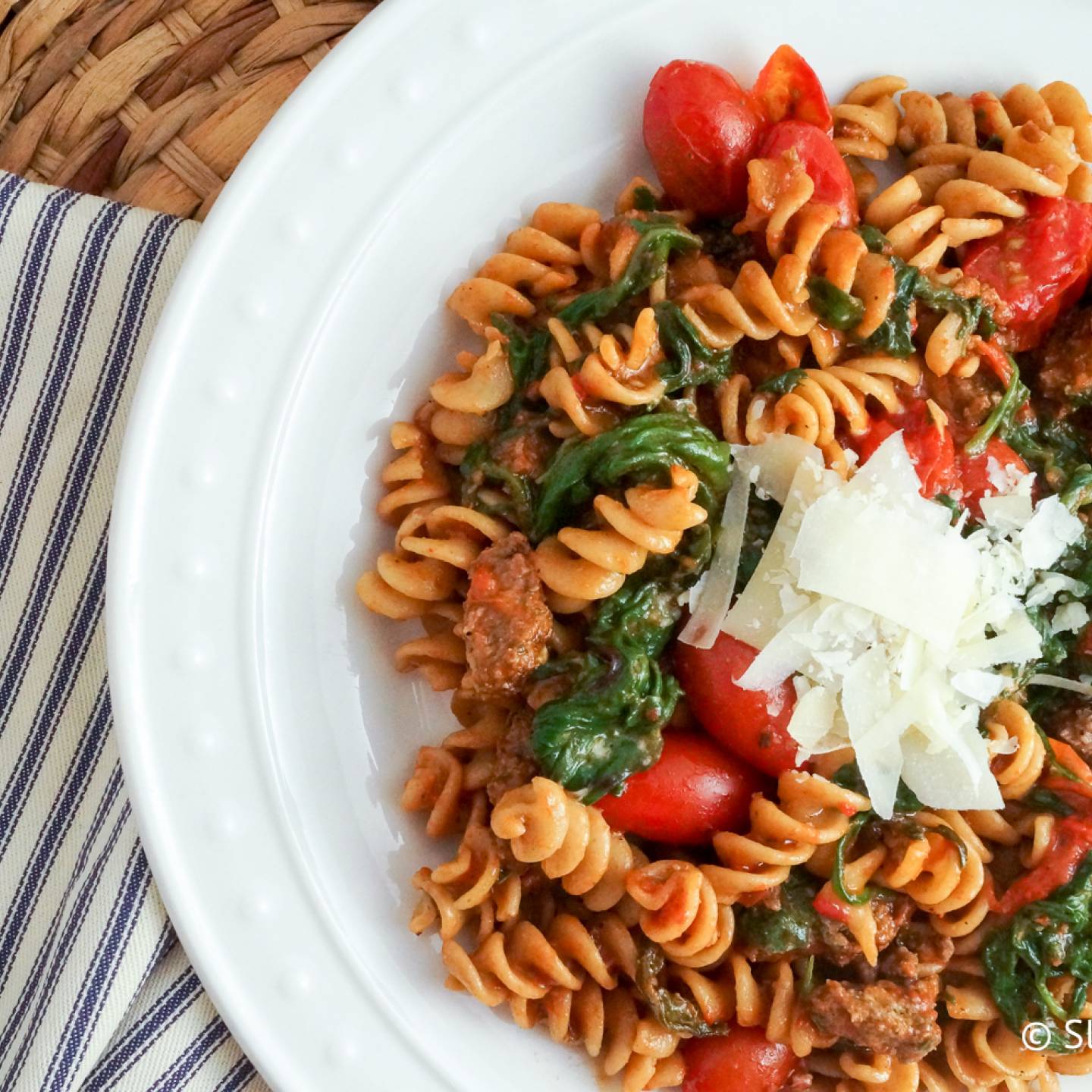 Sausage Arrabbiata pasta with fresh cherry tomatoes and spinach on a plate.