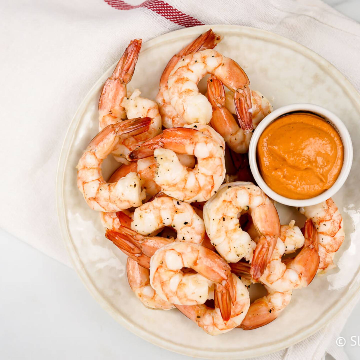 Shrimp cocktail with a small bowl of sauce on a white plate.