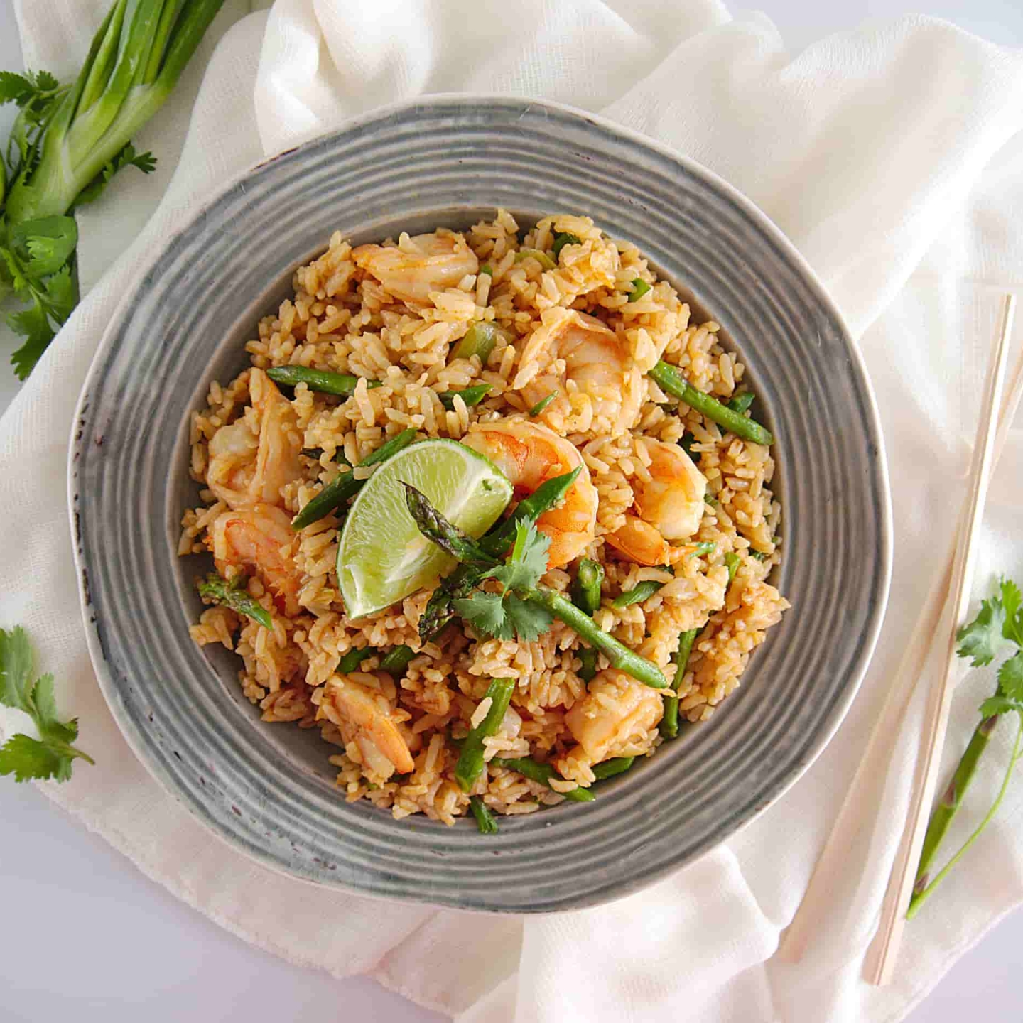 Shrimp fried rice with asparagus, cilantro, and a lime wedge in a bowl.