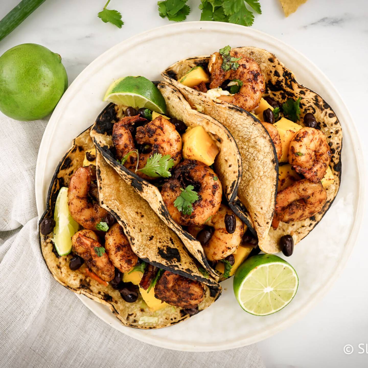 Shrimp tacos served with mango salsa served in corn tortillas with fresh lime wedges. 