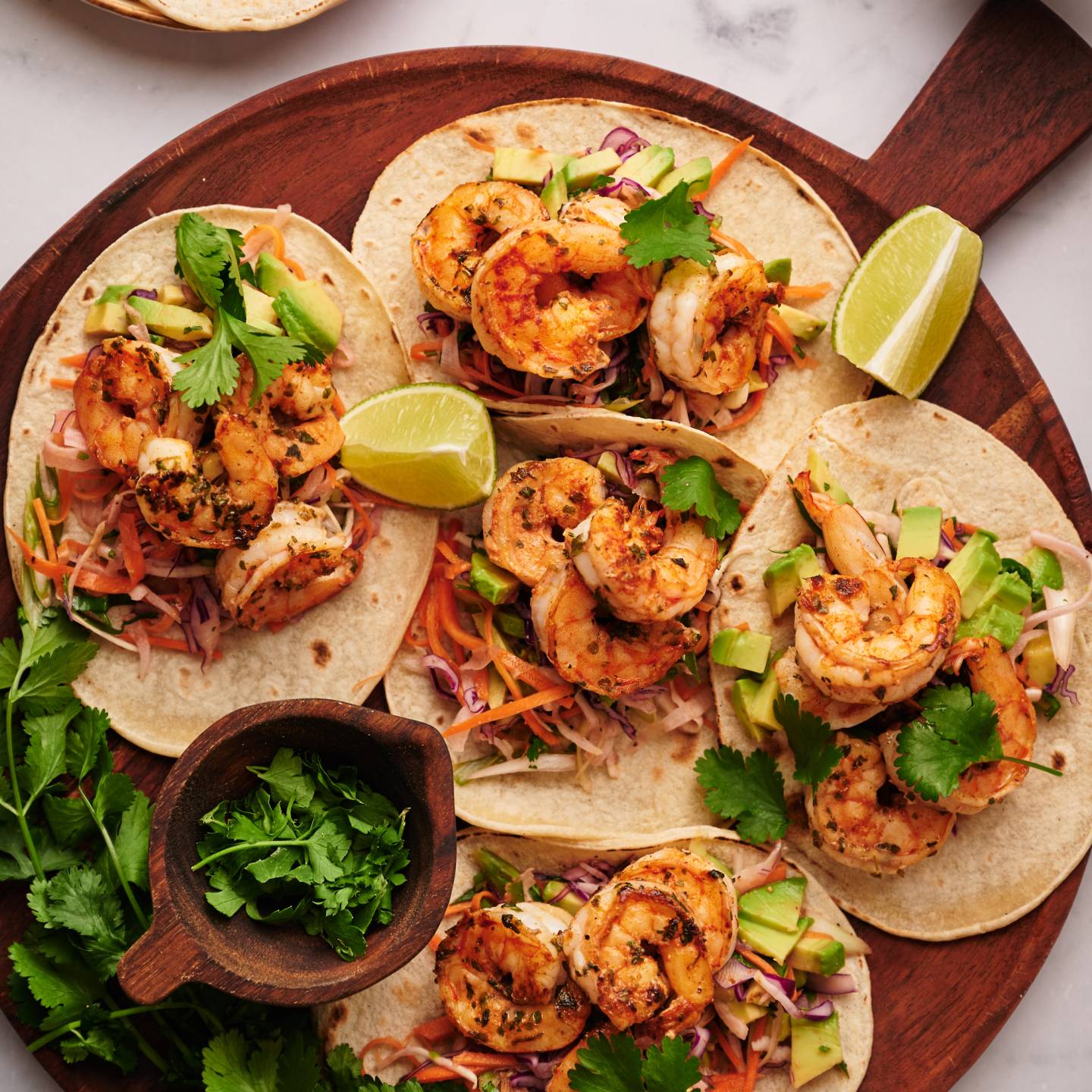 Shrimp tacos with slaw served on corn tortillas with avocado, lime, and fresh cilantro.