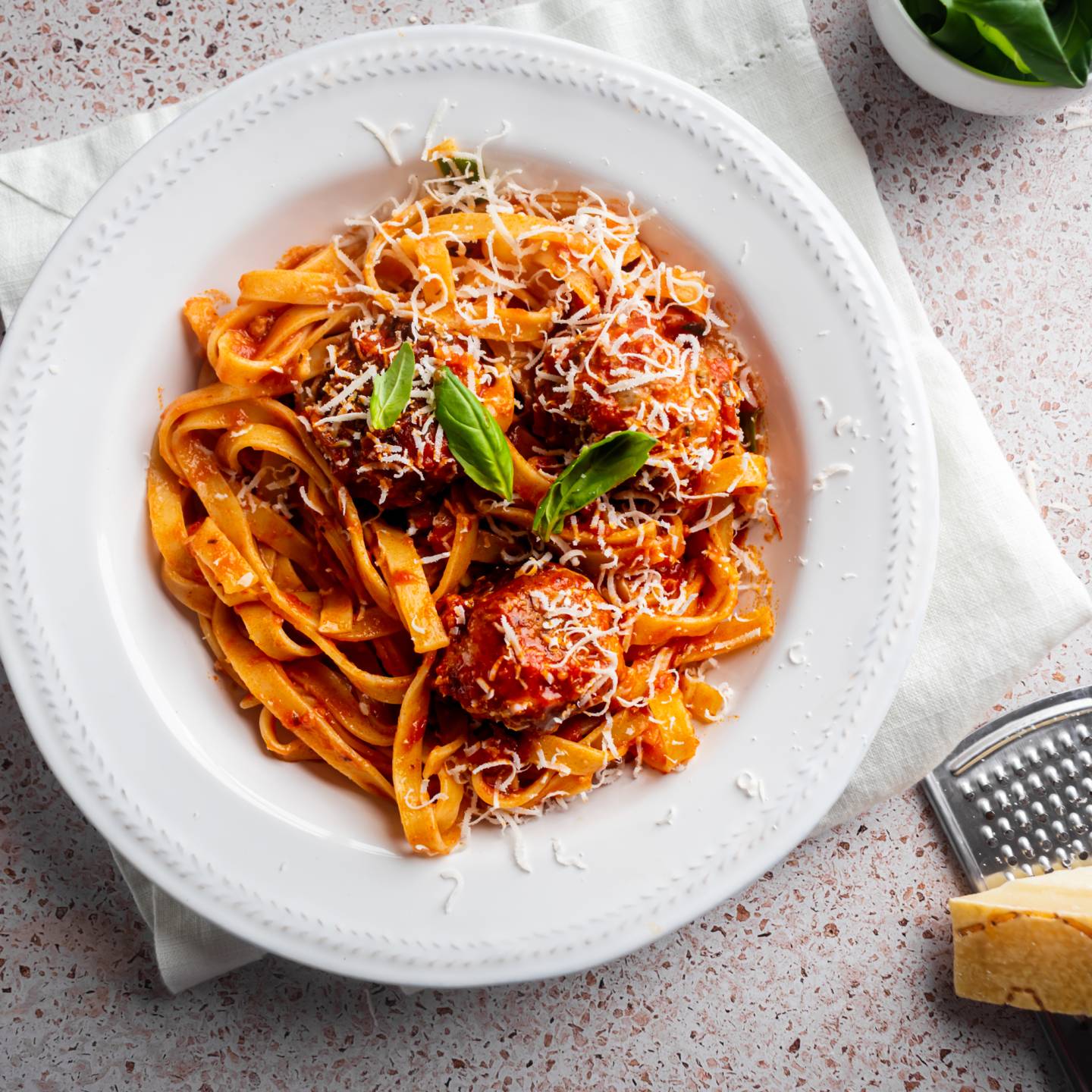 Slow cooker Italian meatballs served with pasta, parmesan cheese, and fresh basil.