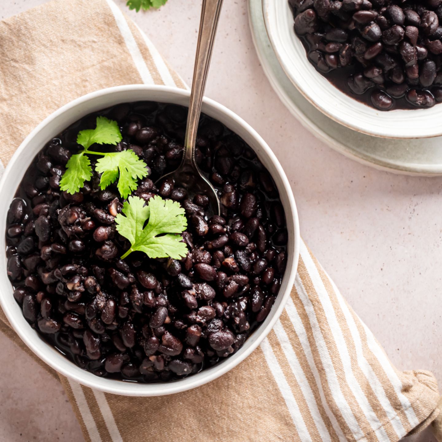 Slow cooker black beans served in two bowls with cilantro and a spoon.