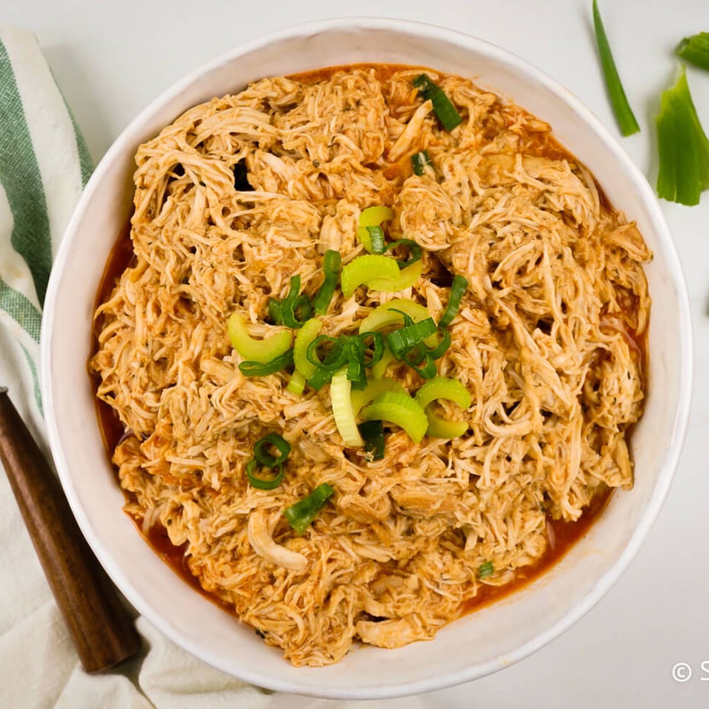 Slow cooker buffalo chicken shredded in a bowl with diced celery and buffalo sauce.