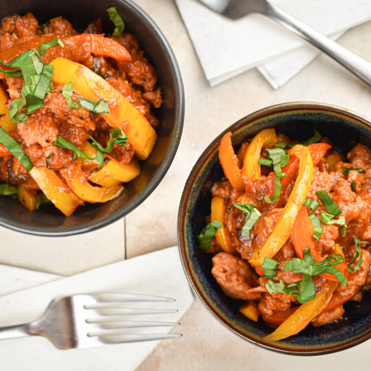 Slow cooker sausage and peppers in a homemade tomato sauce in two bowls with forks.