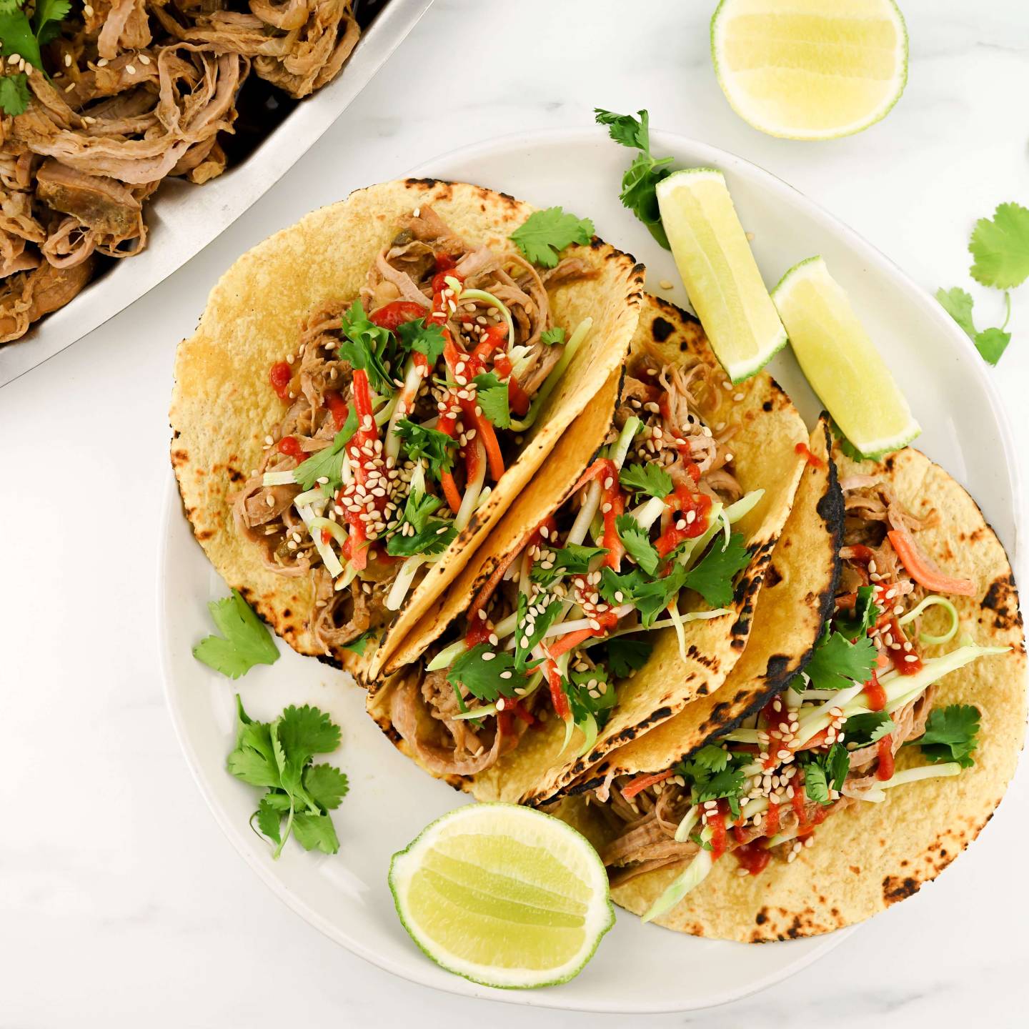 Slow Cooker Korean Pork served in corn tortillas with slaw and hot sauce.