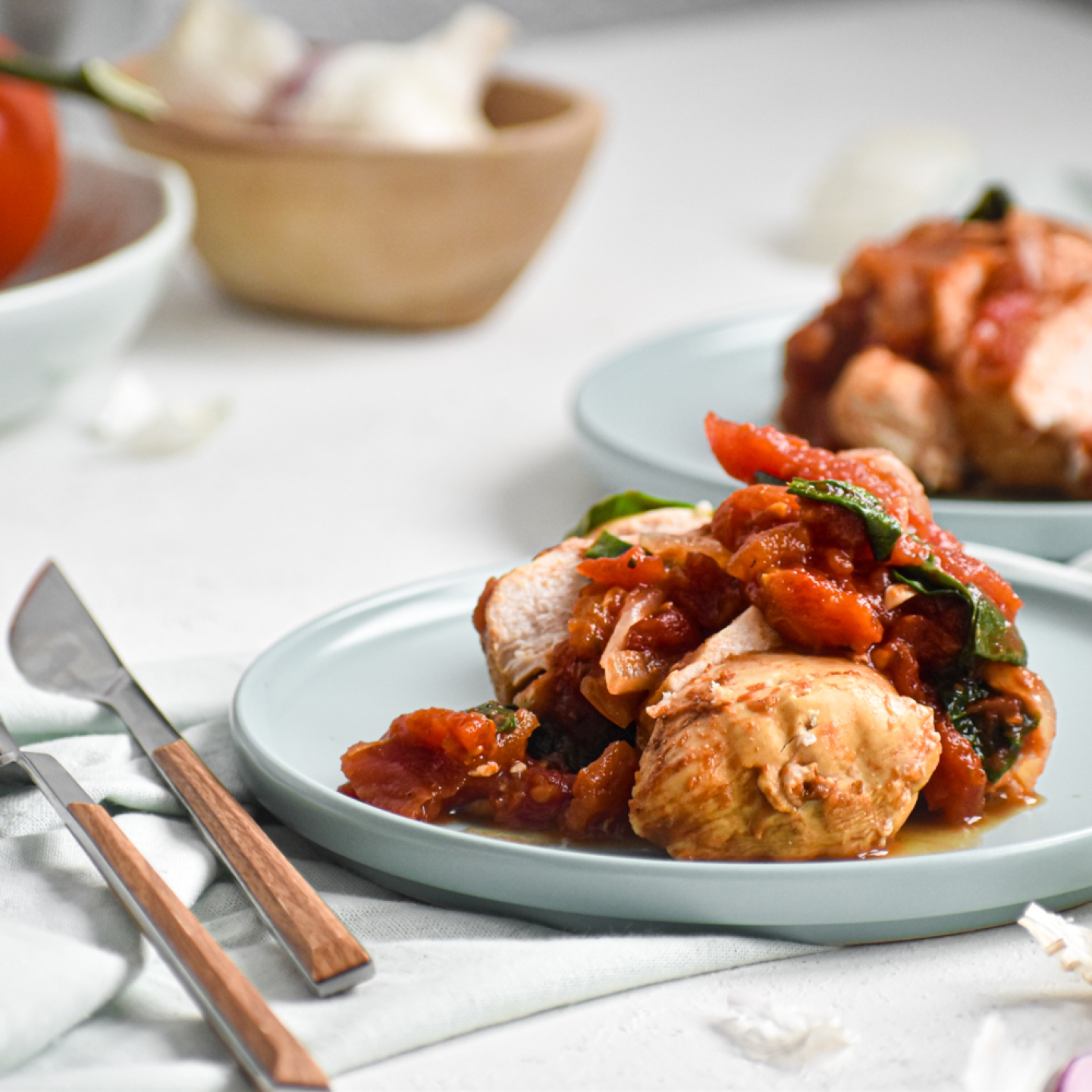 Slow cooker tomato balsamic chicken sliced and served with spinach and basil on a plate.