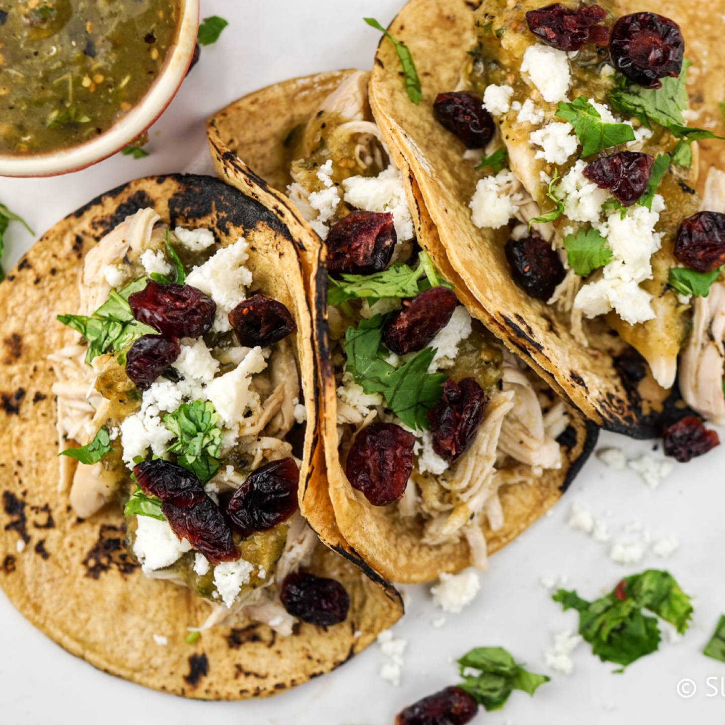 Slow cooker turkey tacos served in corn tortillas with shredded turkey, green salsa, cotija cheese, and dried cranberries.